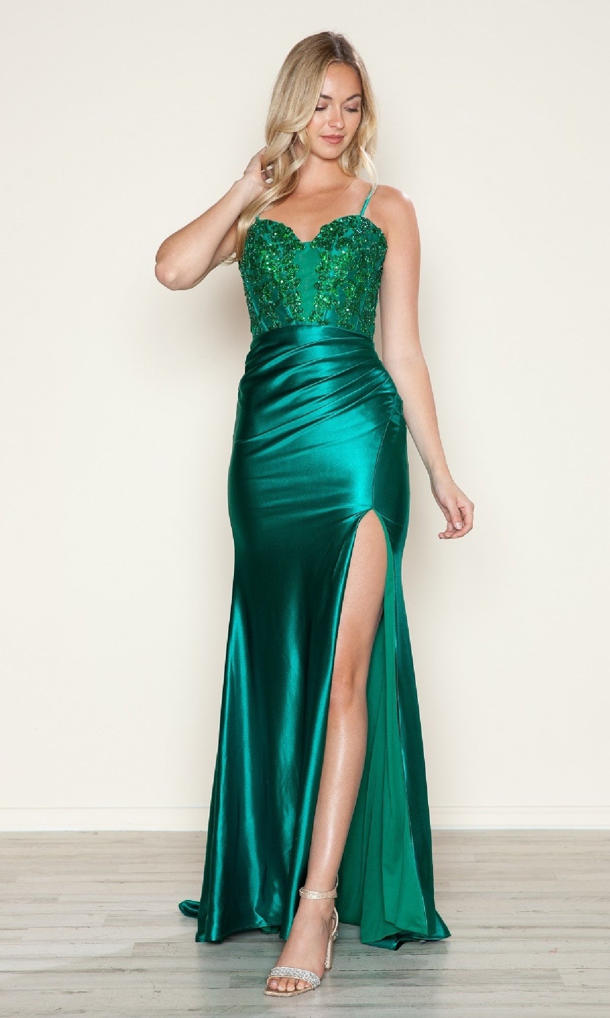 A woman models the Poly USA 9616 beaded-bodice long prom dress in emerald, featuring a fitted sparkly corset bodice, thigh-high slit, and thin straps, set against a plain light background.